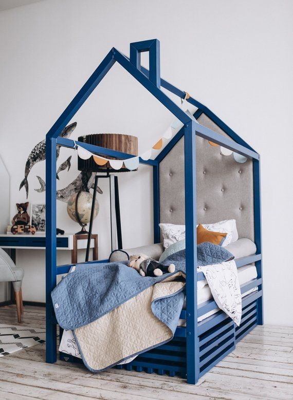 Cama azul con forma de casa en una habitación infantil